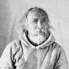 Portrait photographique de Mallikee vêtu d'un parka en peau d'animal et de mitaines en fourrure; cette photo a été prise dans un studio, puis placée dans un cadre de forme ovale, Fullerton, Nunavut, 1904-1905