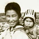 Photo d'une femme inuite portant son enfant dans un porte-bébé, lieu inconnu, Nunavut, été 1952