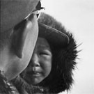 Photo d'un homme et d'un garçon inuits se faisant tirer par un traîneau à chiens, lieu inconnu, Nunavut, 1962