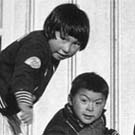 Photo de quatre enfants inuits jouant au sol devant un bâtiment, lieu inconnu, Nunavut, vers les années 1950