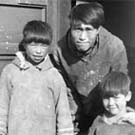 Photo d'un homme et de deux enfants inuits debout sur le seuil d'une maison, lieu inconnu, Nunavut, sans date