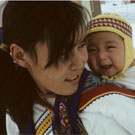 Colour photograph of a young Inuit mother carrying her infant in a baby-pouch, Igloolik (Iglulik), Nunavut, May 1965