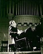 Photograph of Glenn Gould, seated at his piano and leaning back in his chair, 1956