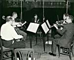 Photograph of Glenn Gould, facing a string quartet on stage in an empty hall